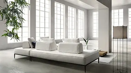Divano modulare dal design contemporaneo, rivestito in tessuto nei toni del grigio chiaro, con sedute ampie e linee essenziali.