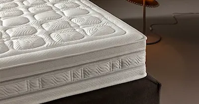 Materasso con copertura bianca, posizionato in una camera da letto ben illuminata.