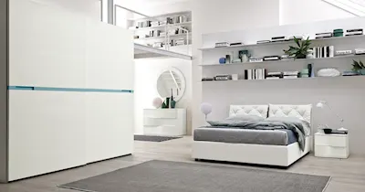 Interno di una camera da letto con arredi bianchi e dettagli blu, per un design elegante e luminoso.